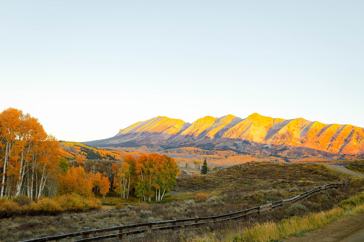 A bright fall landscape in Gunnison, Colorado, captured in 2025, showcasing golden and orange aspens glowing across the valley beneath rugged mountain peaks.