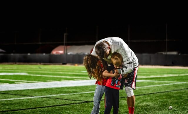 A dad hugs his children during a lacrosse game.