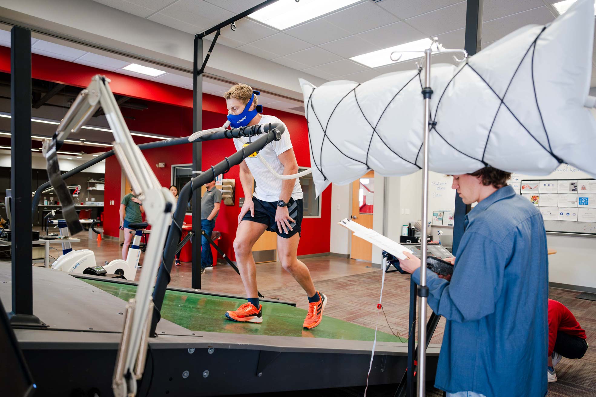 A student wears a VO2 mask as he walks on an inclined treadmill in a lab.