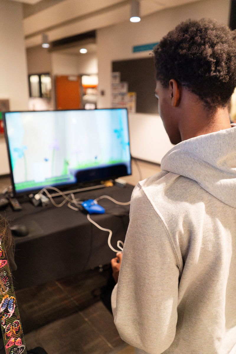A person in a hoodie stands facing a television screen.