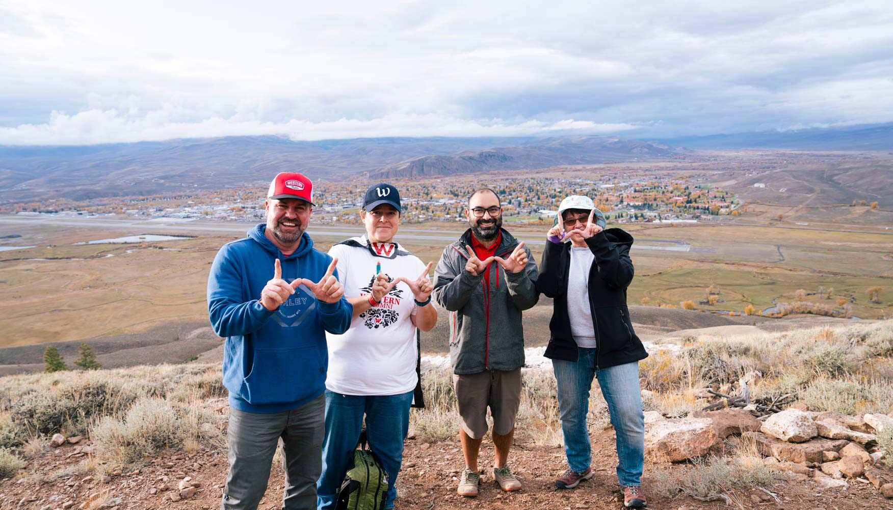 Four Western alumni hold their hands up in the shape of Ws for a photo while standing on W Mountain for the Lighting of the W.