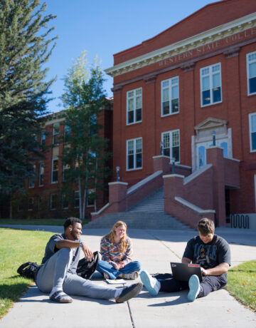 A group of three students sit on Taylor Lawn.