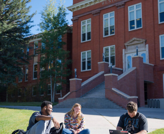A group of three students sit on Taylor Lawn.