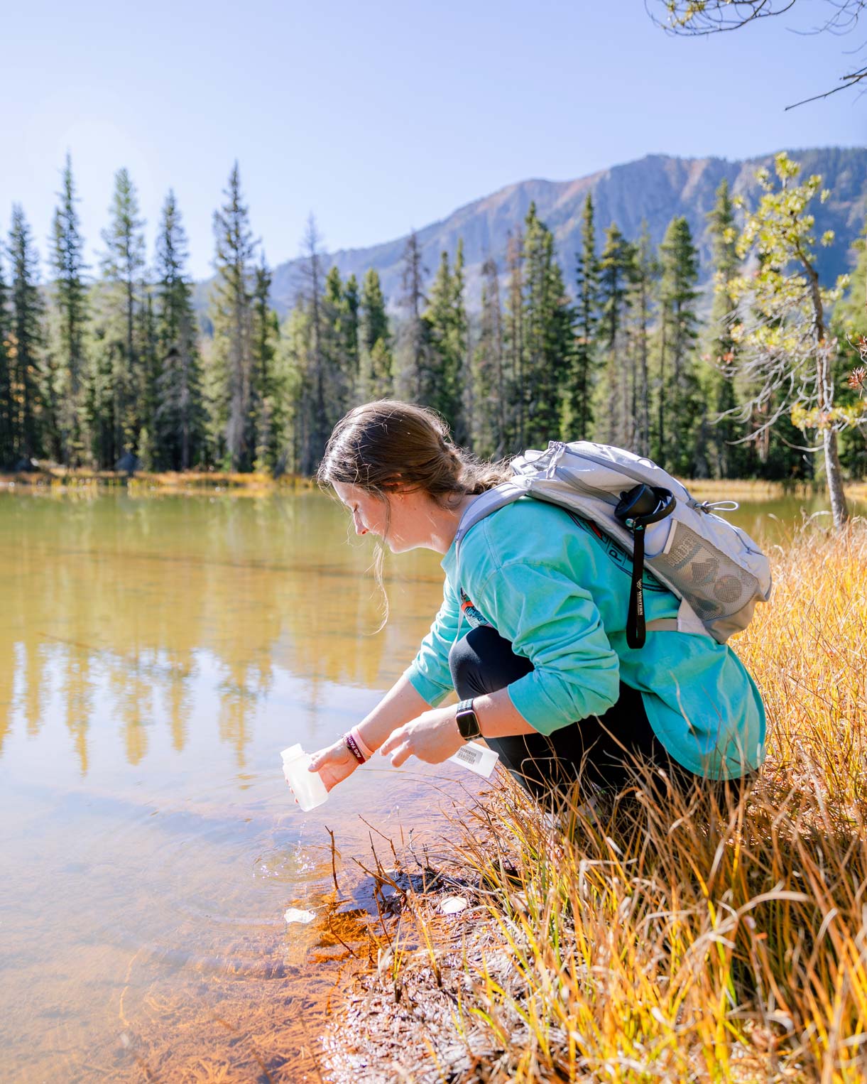 A student kneels as she collects a water sample during a chemistry class.