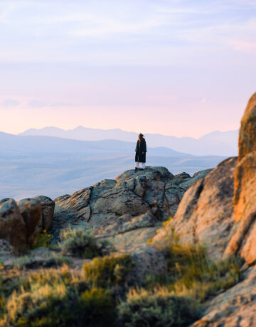 A person in a graduation gown stands atop rocky terrain.