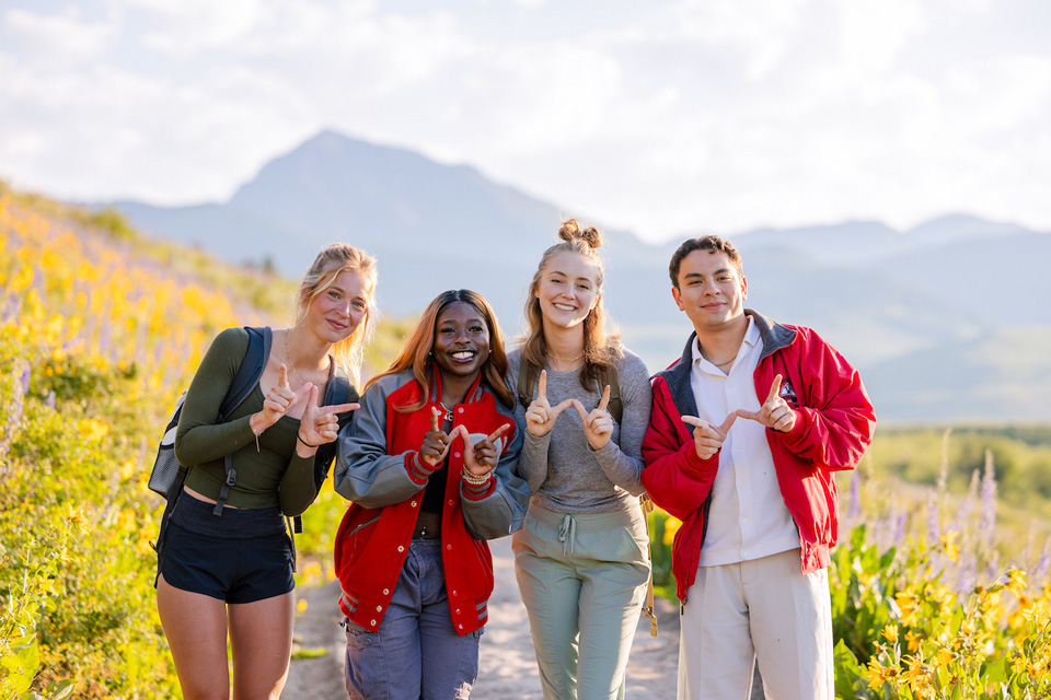 Four students smile in front of Teocalli at sunrise making a W with their hands.