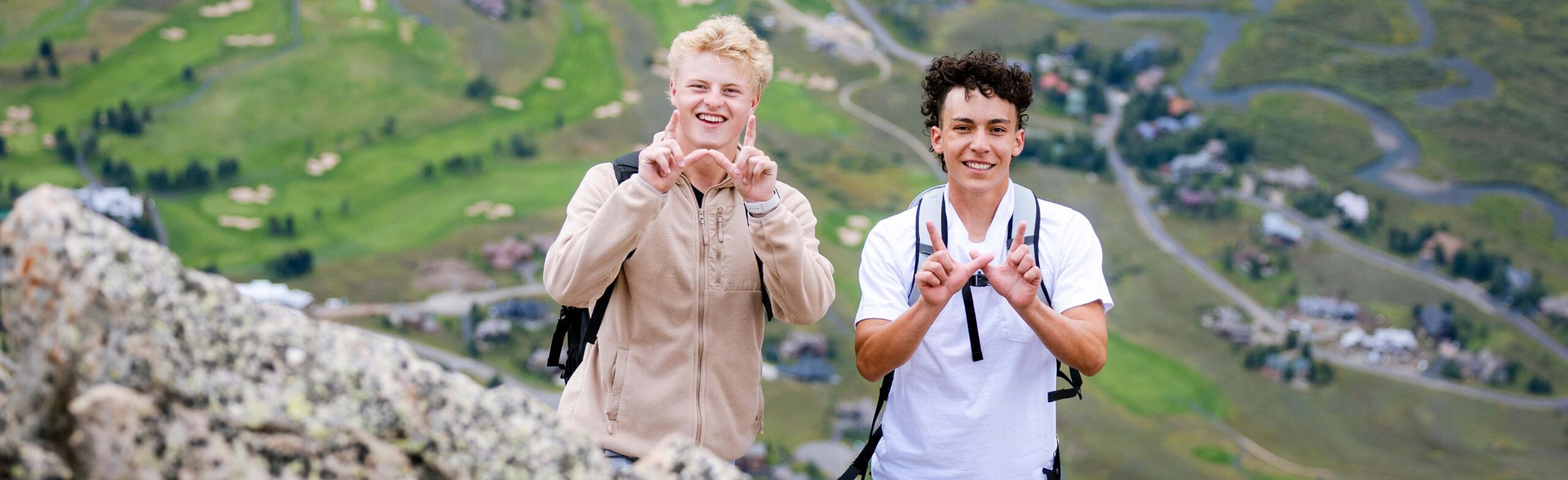 2 students hold up Ws while hiking to the summit of Mt. Crested Butte during university day.