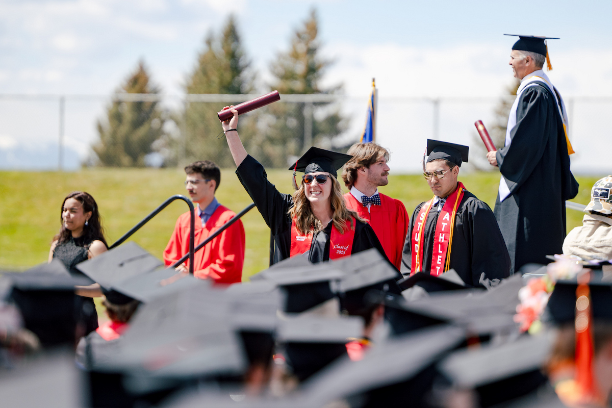 A graduate holds her diploma and waves.