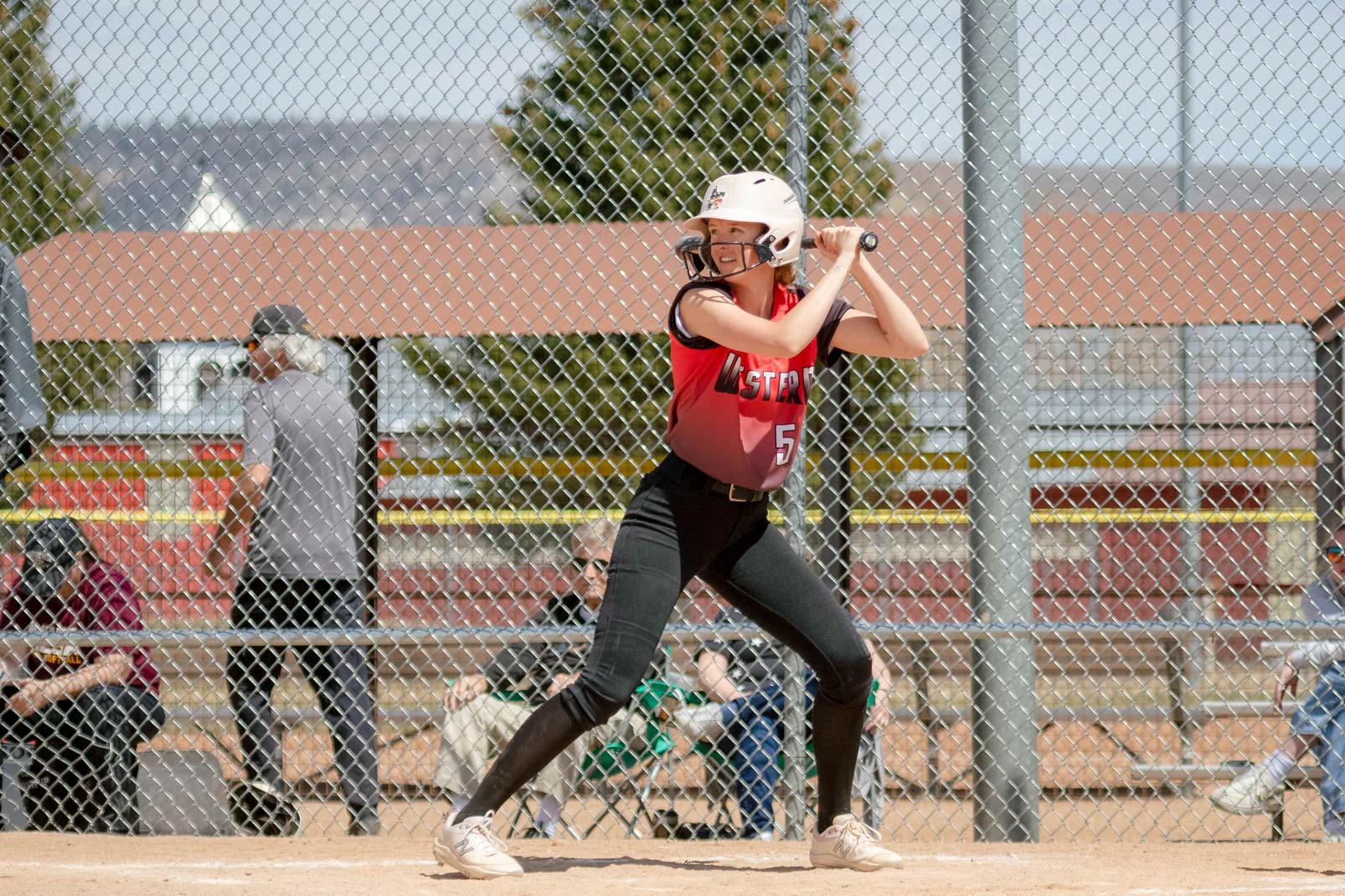 Linnea Baldner prepares to bat during a softball game. She faces the camera as she looks towards the pitcher. She has the bat raised over her left shoulder.